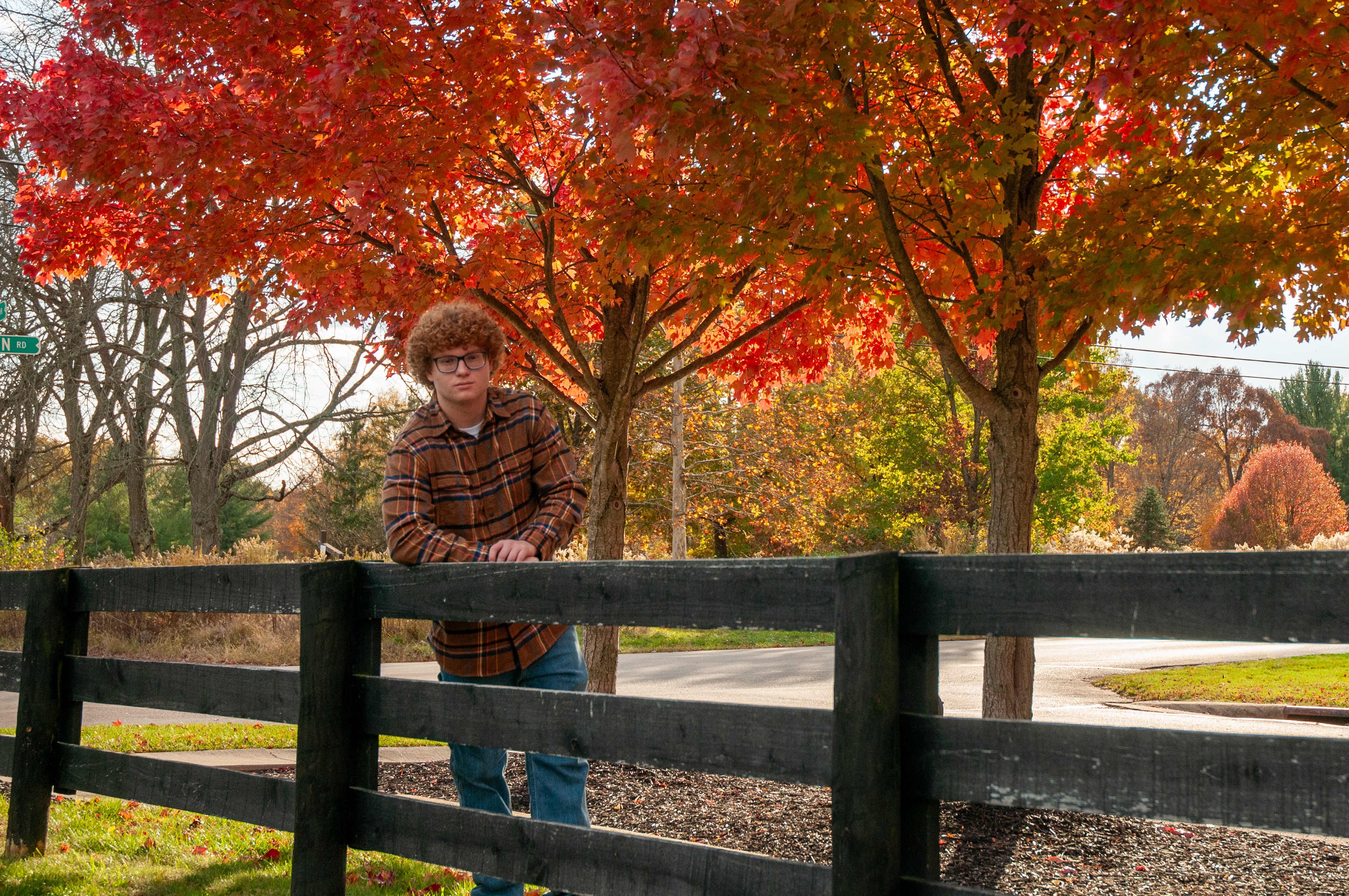 Kellen leaning on a fence with autumn trees